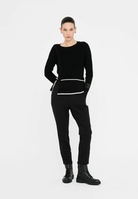 Maglione di lana nero con rifiniture bianche a contrasto, abbinato a pantaloni neri e stivali neri con lacci. Maniche lunghe e dettagli in tessuto testurizzato.