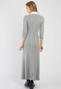 Robe maxi tricotée grise avec un col blanc, des manches trois-quarts et un motif à côtes verticales. Silhouette ajustée avec des détails texturés.