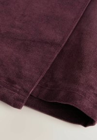 Corduroy stof in een diepe bordeauxkleur, met een geribbelde textuur. De randen zijn netjes afgewerkt met rechte stiksels.