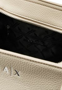 Interno di una borsa in pelle beige con una fodera a motivo nera. Tasca con zip all'interno con un'etichetta che legge "A|X ARMANI EXCHANGE."