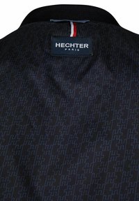 Schwarze Jacke mit geometrischem Muster in Dunkelblau. Beinhaltet ein Etikett mit der Aufschrift "HECHTER PARIS" und ein Dreistrich-Akzent am Kragen.