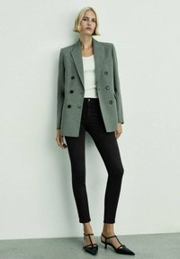 Double-breasted gray blazer with black buttons, white ribbed tank top, black skinny jeans, and black pointed-toe heels. Simple, structured design.