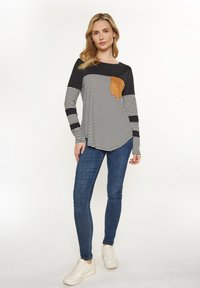 Langärmliges gestreiftes Hemd in Schwarz und Weiß mit einer Tasche aus braunem Wildleder. Kombiniert mit blauen Denim-Jeans und weißen Sneakers. Glattes Material.