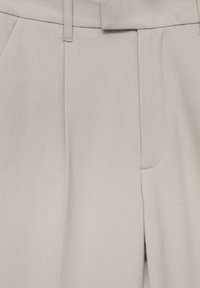 Pantalon beige en tissu lisse, avec des coutures détaillées, des poches avant et une coupe droite.