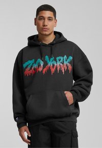 Black hoodie featuring a colorful dripping "Zoo York" graphic. Made of soft material, with a front pocket and adjustable hood.