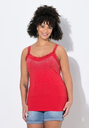 Top rosso senza maniche con rifiniture in pizzo, decorato con borchie argentate che sfumano dal alto verso il basso. Abbinato a pantaloni corti in denim arrotolati.