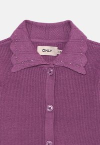 Cardigã roxo canelado com gola scalloped, apresentando pequenas strass decorativas e botões roxos na frente. Etiqueta da marca visível.