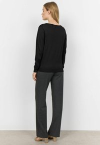 Maglione nero a maniche lunghe e scollatura ampia, abbinato a pantaloni grigio carbone a righe sottili. Il tessuto sembra liscio e morbido.