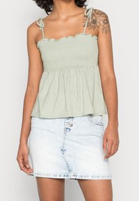 Top verde claro con fruncidos y escote con volantes, con tirantes ajustables, combinado con una falda corta de mezclilla azul claro con cierre de botón.