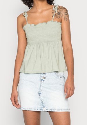 Top smock verde chiaro con scollatura arricciata e spalline regolabili, abbinato a una mini gonna in denim azzurro chiaro con chiusura a bottoni.