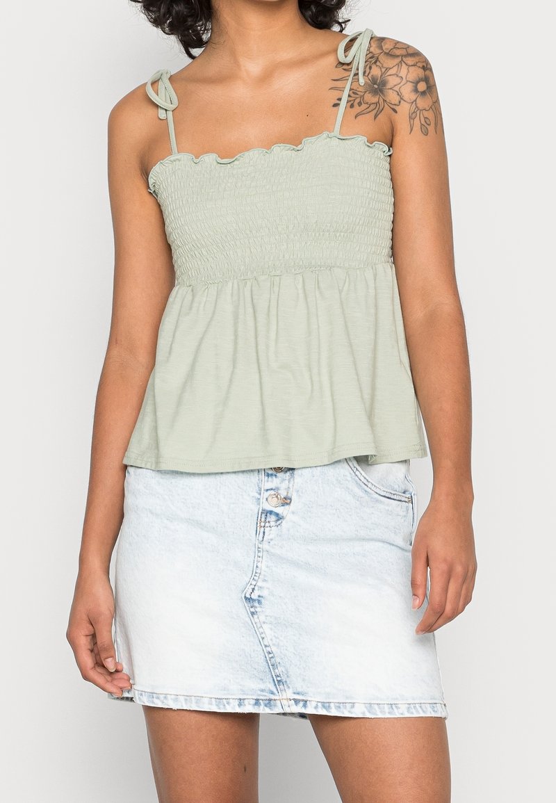Top verde claro con fruncidos y escote con volantes, con tirantes ajustables, combinado con una falda corta de mezclilla azul claro con cierre de botón.