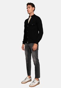 Cárdigan negro de botones con cuello redondo, tejido texturizado, dos bolsillos en el pecho, combinado con jeans grises y zapatillas blancas.