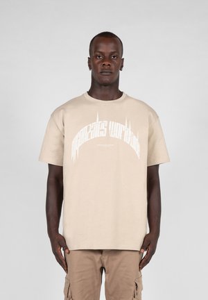 Beige bomulds t-shirt med korte ærmer og rund hals, med hvid grafisk tekst centreret på forsiden. Glat tekstur.