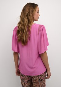 Blusa rosa de manga corta con detalle texturizado en los hombros, hecha de una tela ligera. La parte posterior presenta un escote redondeado y un corte relajado.