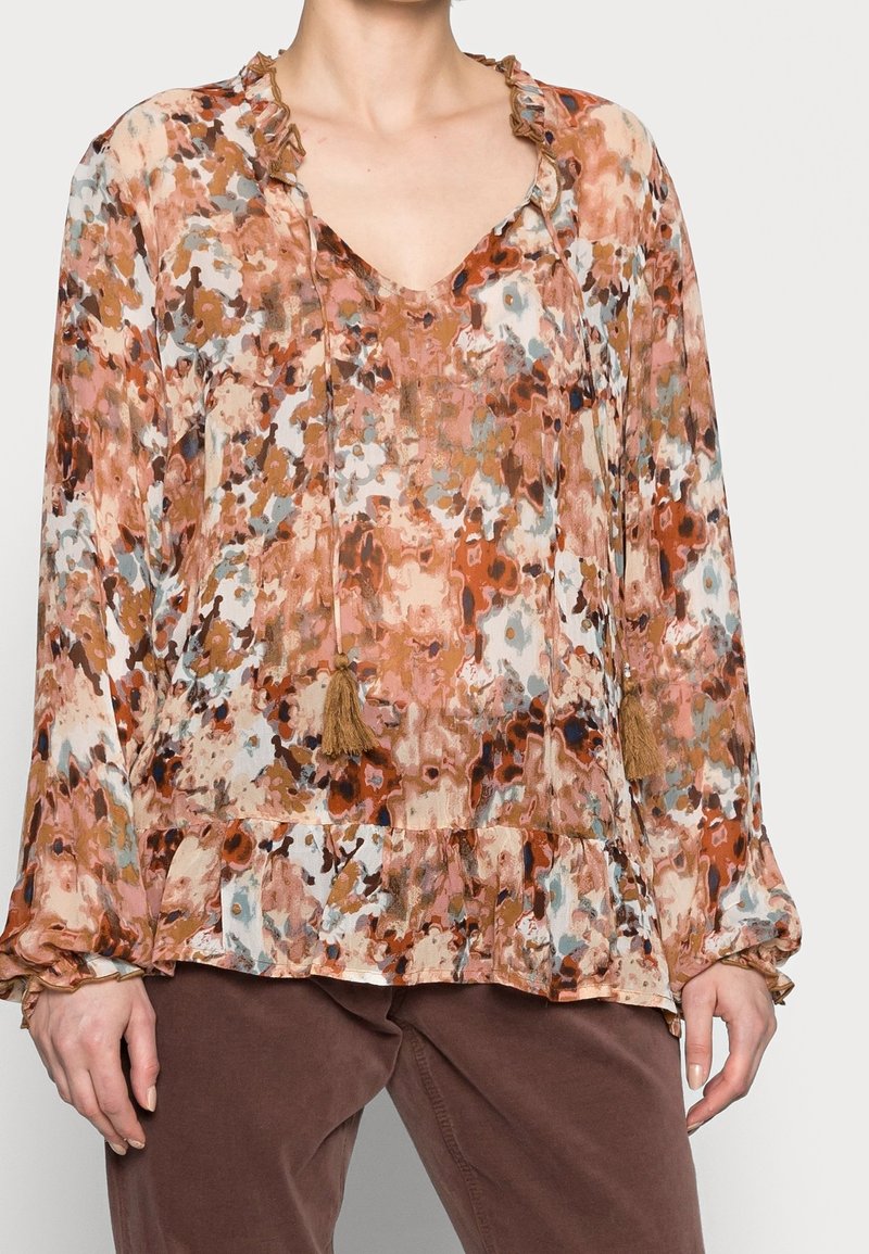 Blusa floral en tonos de marrón, naranja y crema. Presenta un escote en V, un cuello con volantes y detalles de borlas en los lazos. Tejido texturizado.