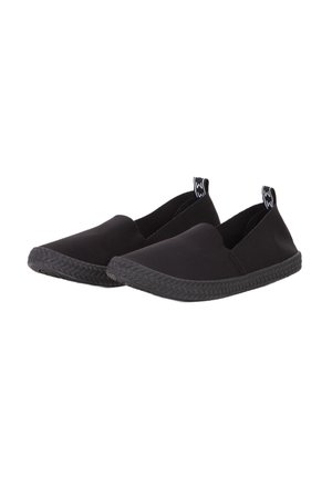 Zapatos negros sin cordones con un upper de tela suave y una suela de goma tejida negra; presentan un diseño minimalista sin acentos o patrones visibles.