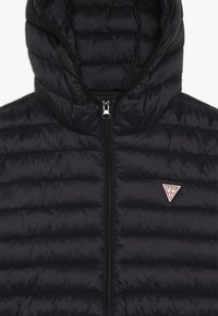 Svart puffjacka med huva, med kviltad textur, frontdragkedjestängning och en triangulär logotyp på bröstet.