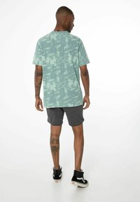 T-shirt verde chiaro a maniche corte con motivo marmorizzato, abbinato a pantaloni corti grigio scuro. Presenta una vestibilità rilassata e orlo arrotolato.