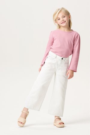 Roze ribbel top met lange mouwen en flared manchetten, gecombineerd met witte high-waisted wijde jeans en tan gekleurde chunky plateau sandalen.