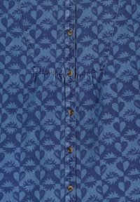 Chemise en denim bleue avec un motif de cœurs et de feuilles, fermeture à boutons à l'avant avec des boutons marron, texture douce.