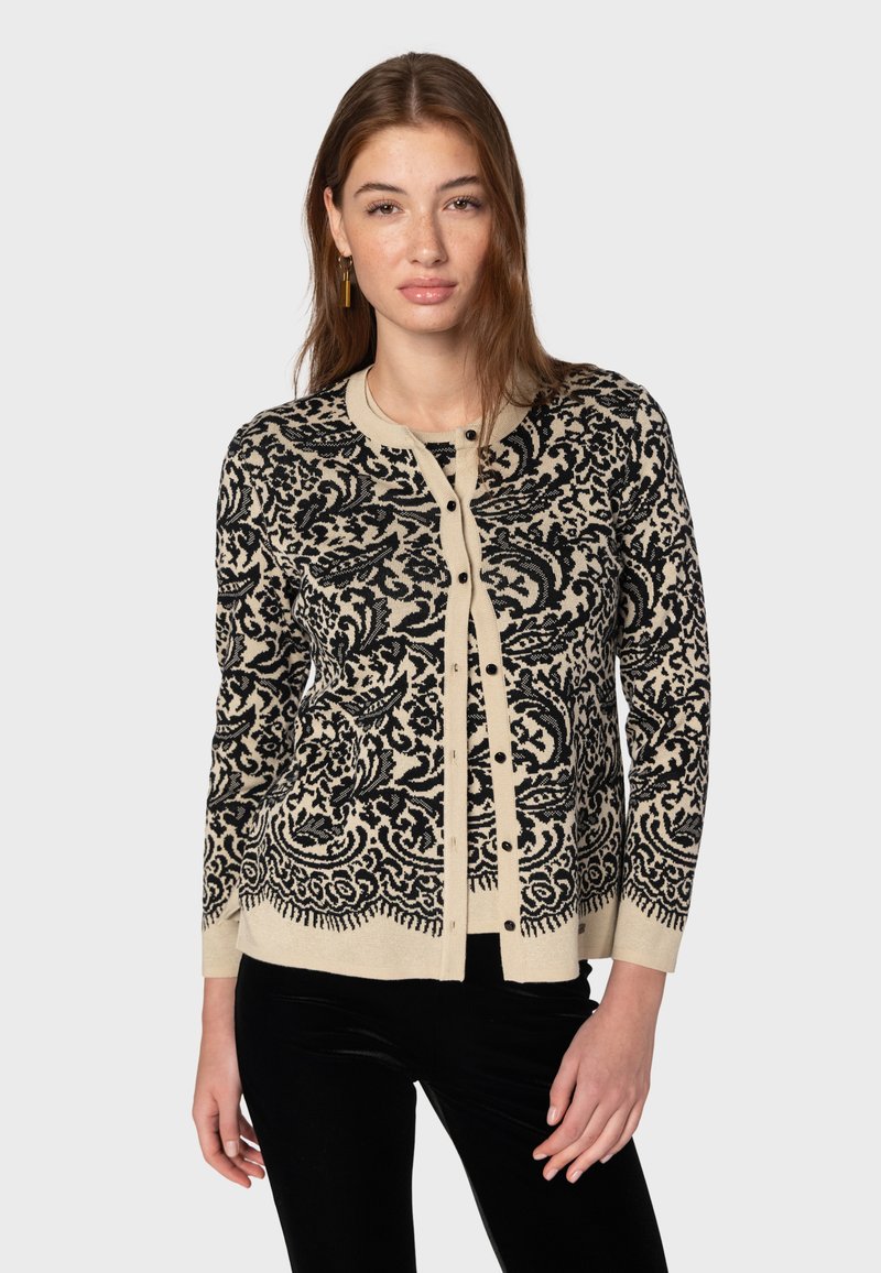 Svart och beige mönstrad kofta med långa ärmar, rund halsringning och knäppning fram. Designen har intrikata svängningar och blommotiv.