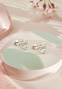 Hjärtformade silverörhängen med utskuret blommönster och studsbackar, med en polerad yta och subtila glittrande detaljer.