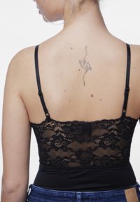 Černá krajková podprsenka s nastavitelnými ramínky, zdobená květinovými vzory na zádech, v kombinaci s přiléhavým černým body.