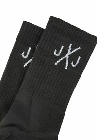 Black socks made of soft, textured fabric featuring a ribbed cuff and white logo on the upper side.