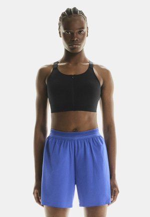Black sports bra with adjustable straps and front zipper; paired with loose-fitting royal blue shorts featuring an elastic waistband.