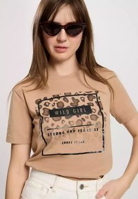 Beżowa bawełniana koszulka z nadrukiem w panterkę oraz czarnym napisem "WILD GIRL STRONG AND FEARLESS" w prostokątnym obramowaniu.