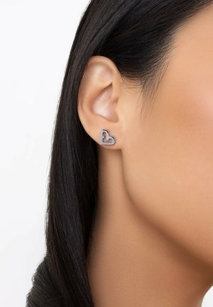 Herzförmige Ohrringe aus Silber mit einer erhabenen Kontur, die eine glatte Oberfläche und ein modernes Design bieten. Sie passen sich eng an das Ohrläppchen an.