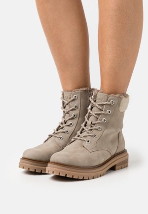 Beige suede ankle boots with faux fur trim, round toe, lace-up design, and rubber sole featuring a rugged tread pattern.