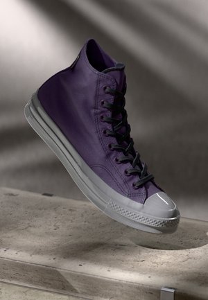 Hoge paarse canvas sneaker met zwarte veters, rubberen neuskap en doorzichtige zool, met een gladde textuur en een minimalistisch ontwerp.