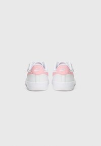 Baskets synthétiques blanches avec des accents rose clair et une languette au talon, présentant une texture lisse et un design à bout rond.