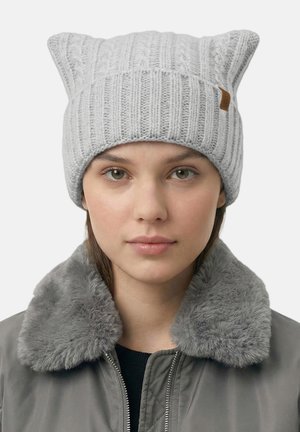 Graue gestrickte Mütze mit Katzenohren-Design, geripptem Muster und einem Lederetikett an der Seite, getragen mit einer grauen Jacke mit Pelzkragen.
