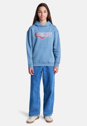 Sweat à capuche bleu clair avec une poche avant, arborant un graphisme audacieux. Associé à un jean large délavé clair et des baskets blanches.