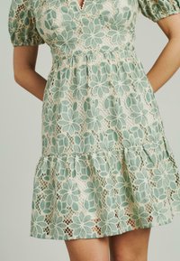 Vestido de manga corta con una sobrecapas de encaje floral en verde menta, falda en capas y cintura ajustada, con un delicado diseño de escote en V.
