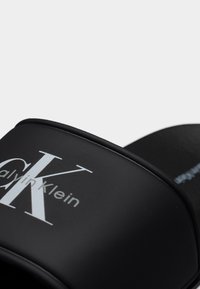 Μαύρο σανδάλι με λουρί, με το λογότυπο Calvin Klein σε λευκό, με λείο ματ φινίρισμα και καμπυλωτές άκρες.