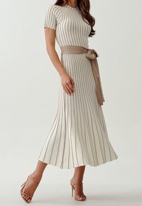 Robe crème jusqu'au genou avec de fines rayures verticales, manches courtes, un corsage ajusté et une ceinture en tissu assorti nouée à la taille.