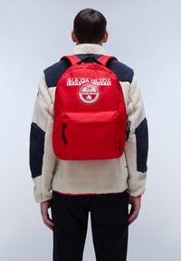 Zaino rosso con una toppa logo anteriore, spallacci regolabili e una tasca con cerniera. Realizzato in tessuto resistente, con una texture liscia e un design funzionale.