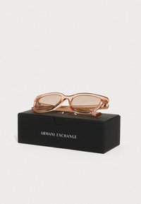 Rosen läbipaistvad prillid, millel on ristkülikuline kuju ja pruunid läätsed, on välja pandud mustal karbil, millel on silt "Armani Exchange".
