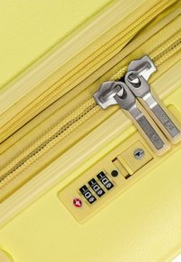 Valigia rigida gialla con una superficie testurizzata, dotata di doppie cerniere, un lucchetto a combinazione e un dettaglio di sicurezza approvato dalla TSA.