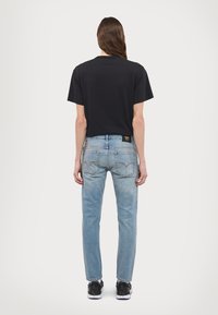 Svart bomull T-skjorte med korte ermer, sammen med lyseblå denimjeans med baklommer og en svart label. Svarte joggesko fullfører antrekket.