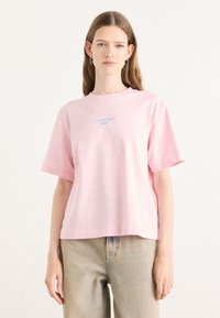 T-shirt di cotone rosa con maniche corte e colletto tondo; presenta un logo ricamato blu "Calvin Klein Jeans" centrato sul petto.