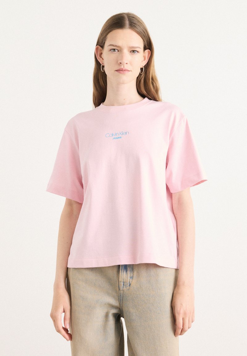 T-shirt di cotone rosa con maniche corte e colletto tondo; presenta un logo ricamato blu "Calvin Klein Jeans" centrato sul petto.