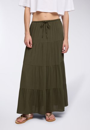 Gonna maxi verde oliva con design a strati, vita elastica e coulisse. Tessuto leggero, abbinata a sandali flat dorati.