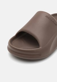 Brun slidesandal lavet af glat materiale med åbent tådesign. Har en tekstureret indersål og præget brandnavn som detalje.