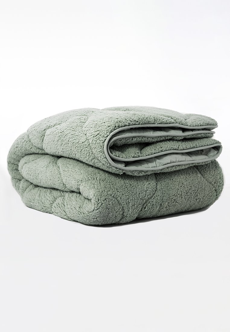 Manta de forro polar verde, textura suave, diseño acolchado, doblada de manera ordenada. Bordes acabados con un trim de tela suave. Ligera y acogedora.