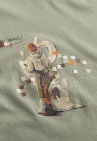 T-shirt grafica in tessuto verde chiaro con una figura dipinta dai capelli corti, intenta a scolpire, circondata da accenti di colore pixelati.