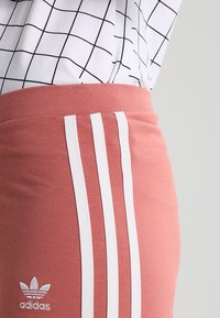 Adidas rosa mjukisbyxor med vit tre-stripes-design. Mjuk tyg med elastisk midjeband. Logo broderad på vänster höft.